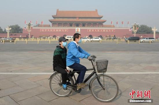 11月3日，北京大气扩散条件转差，空气污染指数持续攀升。据悉，北京已于2日傍晚发布空气重污染黄色预警。图为一对青年佩戴口罩骑车经过北京天安门广场。 中新社记者 崔楠 摄